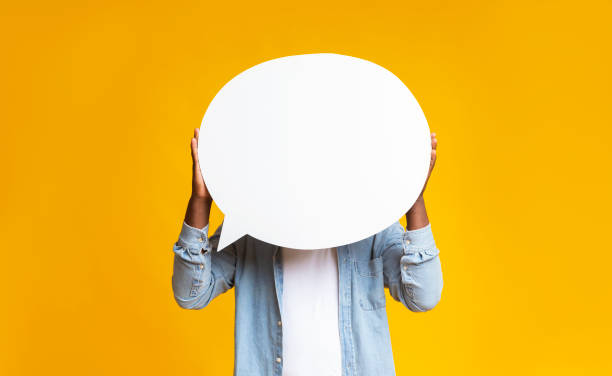 African american man hiding face behind empty speech bubble Unrecognizable black guy holding empty speech bubble in front of his head over yellow studio background, copy space announcement message photos stock pictures, royalty-free photos & images