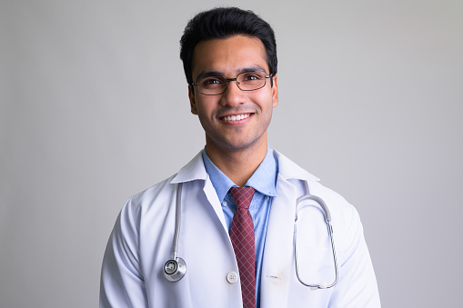 Studio shot of young handsome Indian man doctor against white background