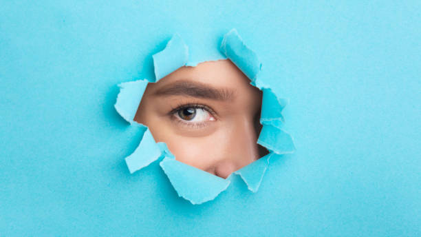 istock Woman looking at camera through torn blue paper 1187319212