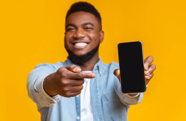 istock Cheerful african guy pointing at smartphone with black screen 1187319318