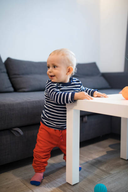 Cute baby holding on to table in living room. Learning to walk stock photo