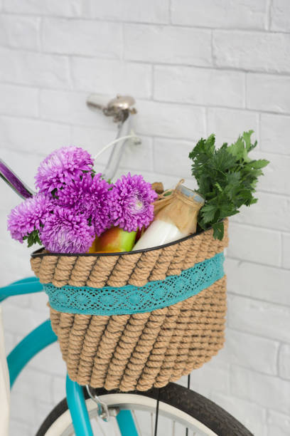 Close up of freshness concept. Wildflowers and organic vegetables in basket on bicycle over white bricks wall background, vertical panorama