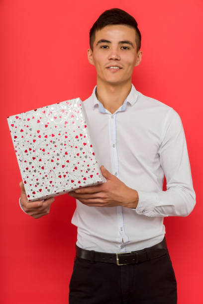 istock Handsome asian businessman holding gift box over red background 1187322672