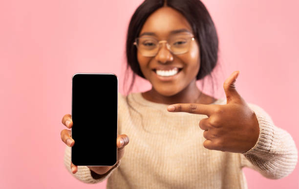 istock Black Lady Showing Phone Blank Screen Standing, Pink Background, Mockup 1187323659