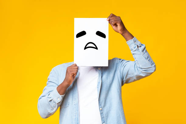 istock African american guy hiding face behind paper with sad emoticon 1187325169