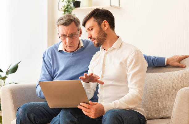 istock Middle-Aged Son Teaching Father To Use Laptop Sitting Indoor 1187325506
