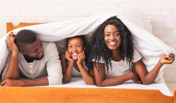 istock Mother, father and daughter hiding under blanket, having fun together 1187328626