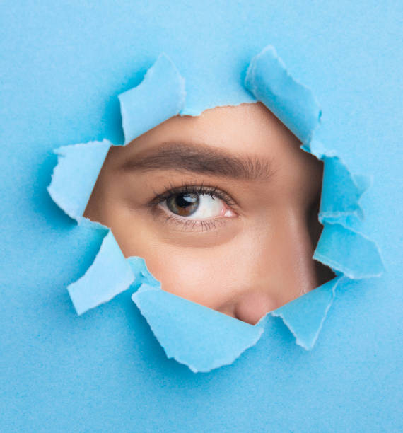 istock Girl looking through blue torn paper, spying 1187330111