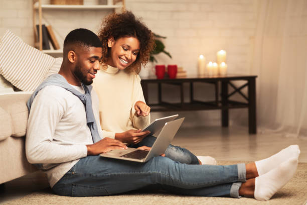 istock Happy african-american spouses browsing internet on gadgets 1187330391