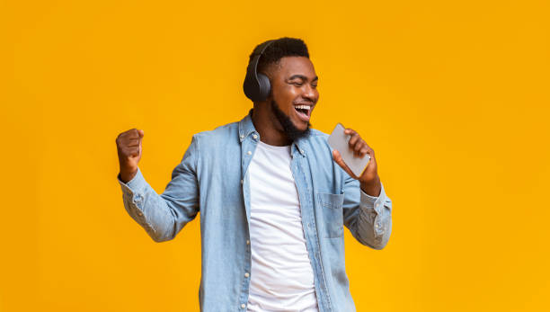 istock Black guy in wireless headphones singing into smartphone like microphone 1187331300
