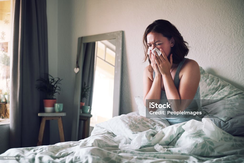 I should have totally gotten that flu shot Shot of an attractive young woman suffering with the flu while sitting on her bed at home Illness Stock Photo