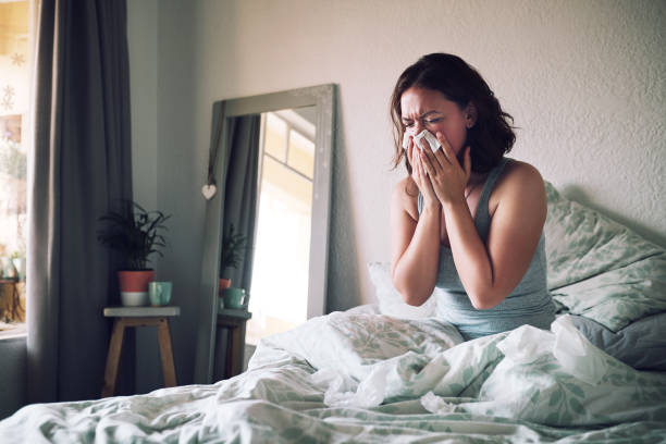 I should have totally gotten that flu shot Shot of an attractive young woman suffering with the flu while sitting on her bed at home blowing nose photos stock pictures, royalty-free photos & images