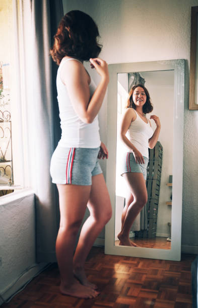 Her self-love level is unmatched right now Full length shot of an attractive young woman admiring herself while standing in front of the mirror in her bedroom at home caucasian appearance stock pictures, royalty-free photos & images