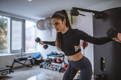 Fit strong young woman lifting weights at gym