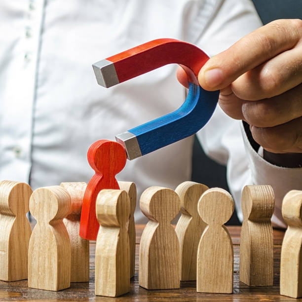istock A man with a magnet pulls a red human figure out of crowd. Identify disloyal, repression, dissent. toxic, non-competent worker. manages the business. Candidate for work, talent. Human resources 1187339855
