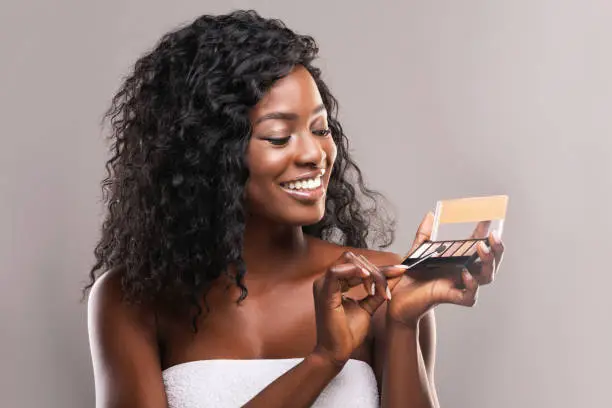Beauty blogger. Attractive afro woman testing new eyeshadow palette over gray background with free space