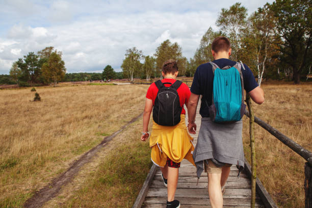 Rear view of a father and his son walking on a wooden footpath on their hiking trip with their backpacks on stock photo