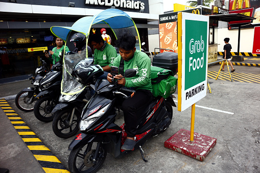 Antipolo City, Philippines - November 8, 2019: Drivers of a popular food delivery service wait for customer orders at a designated parking lot.