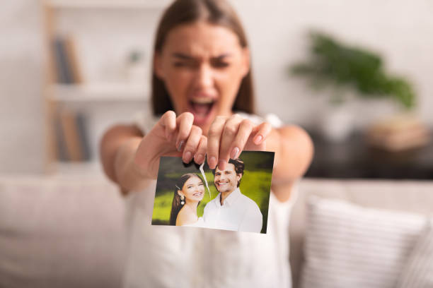 Furious Woman Ripping Wedding Photo Sitting On Sofa Indoor Breakup. Furious Woman Ripping Wedding Photo With Ex-Husband Sitting On Sofa Indoor After Divorce. Selective Focus former photos stock pictures, royalty-free photos & images