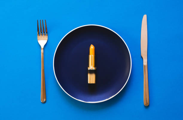 istock Gold lipstick lies on a colored plate on a blue background with a knife and fork 1187343668