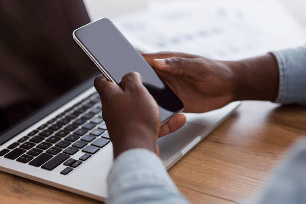 istock Black businessman holding smartphone with black screen and using laptop 1187344810