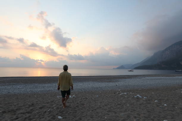 l'homme marche en bas de la plage au lever de soleil - shorts rear view summer beach photos et images de collection
