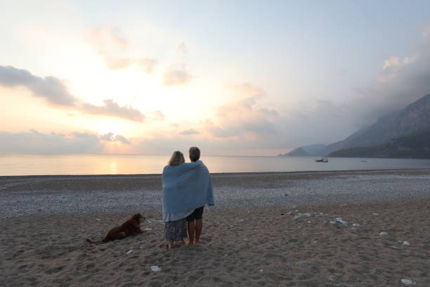 Couple walks down beach with dog at sunrise