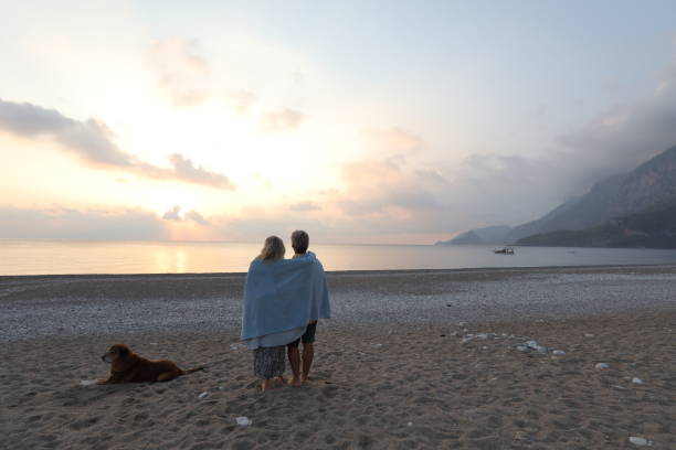 istock Couple walks down beach with dog at sunrise 1187346687