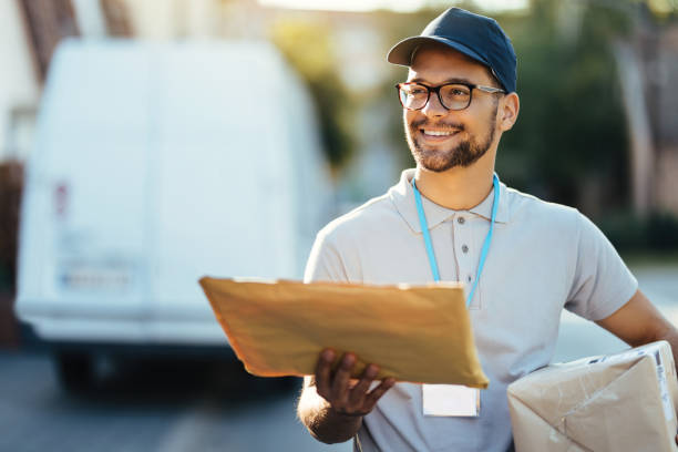 住宅街で配達を行う若い幸せな郵便労働者。 - postal worker ストックフォトと画像