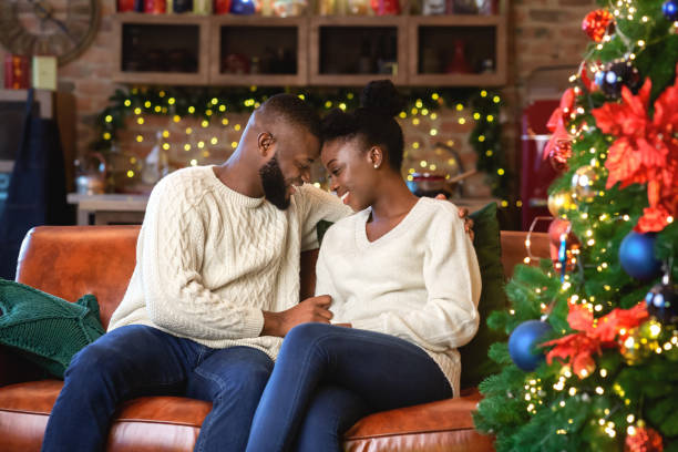 istock Romantic afro couple sitting on sofa near Christmas tree 1187347953