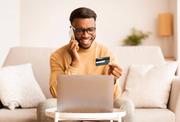 istock Man Talking On Phone Using Credit Card Laptop Sitting Indoor 1187348016