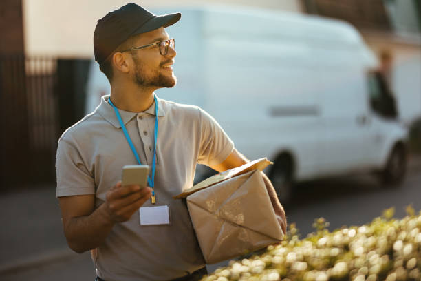 istock Happy delivery man text messaging on mobile phone while carrying packages. 1187348290