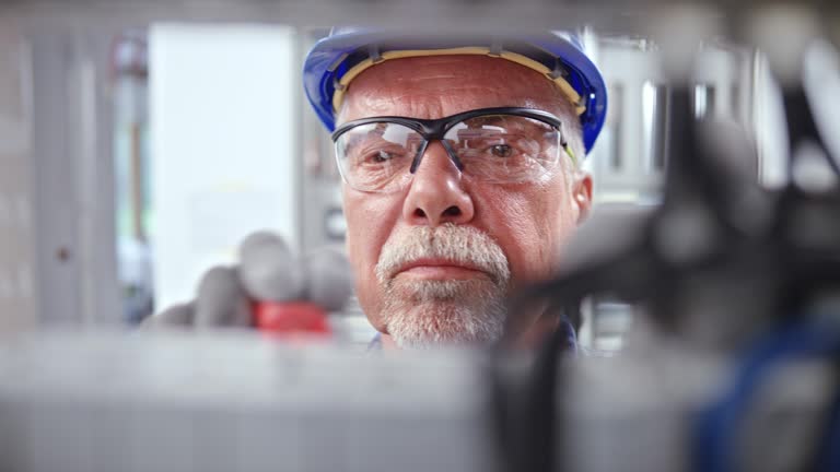DS Face of a senior male electrician connecting wires in the electrical panel
