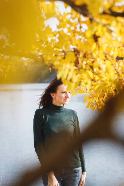 Young woman under yellow tree on lake background.