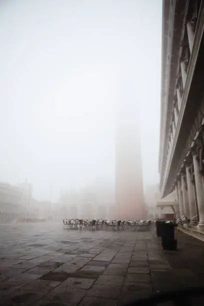 Venice. Italy - October 28, 2019: empty cafe tables and Piazza San Marco on a foggy morning just after the dawn with Campanile lost in mist and everything blurry and out of focus.