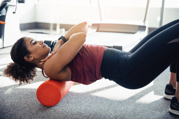 Stretching Her Upper Back young woman stretching her back at the gym, using a foam roller rolling stock stock pictures, royalty-free photos & images