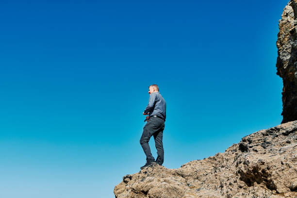 istock Man stood on rocks against a blue sky looking out over unseen view. 1187359307