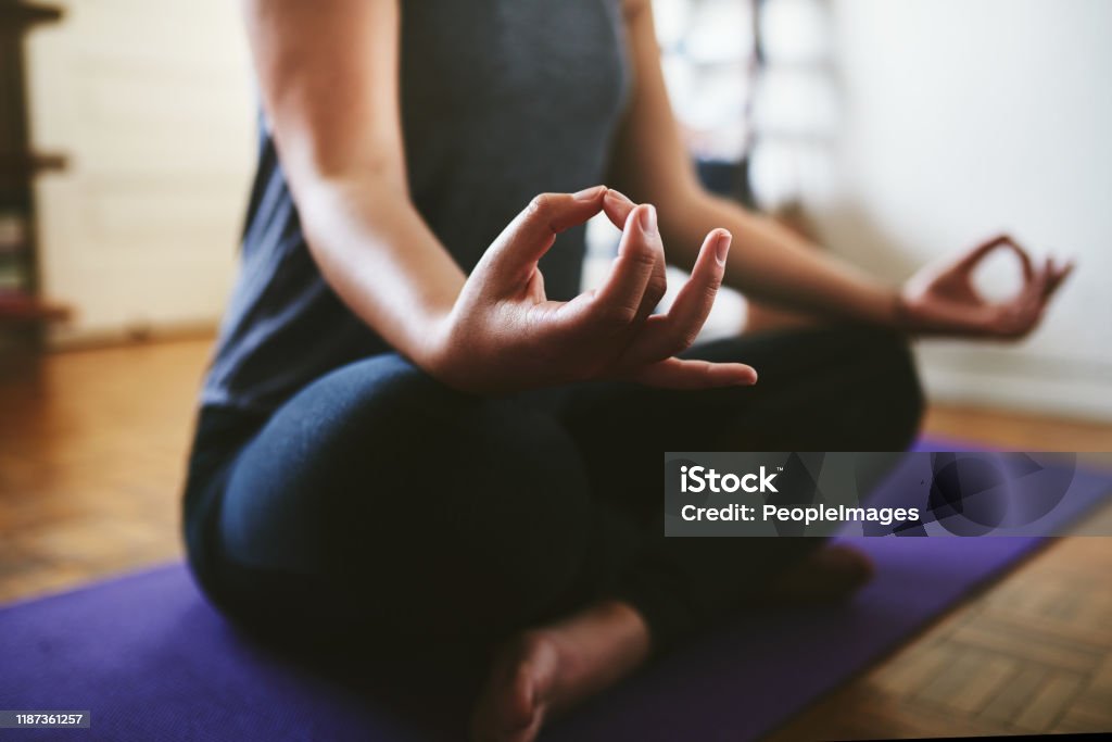 Finding my balance Cropped shot of an unrecognizable woman sitting on a yoga mat and meditating alone in her home Meditating Stock Photo