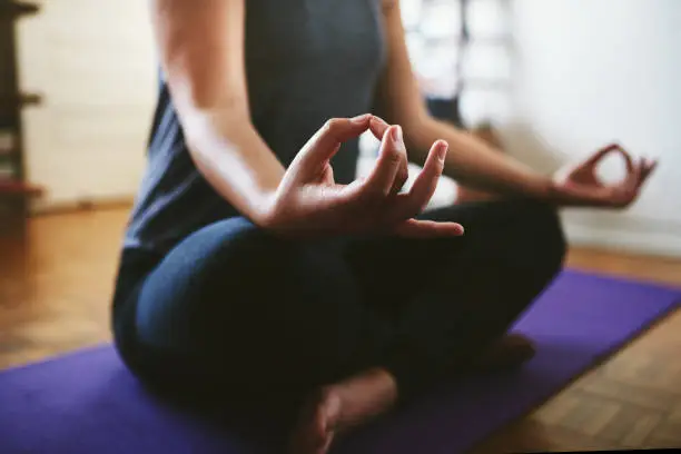 Cropped shot of an unrecognizable woman sitting on a yoga mat and meditating alone in her home