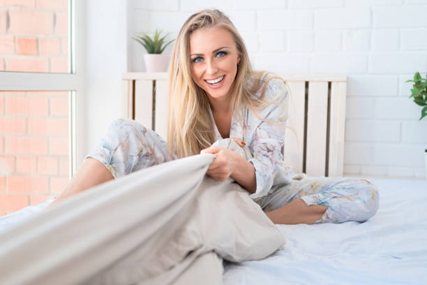 szczęśliwa blondynka śmieje się i ciągnie koc nad sobą. gra w łóżku. - waking up women bedding underwear zdjęcia i obrazy z banku zdjęć