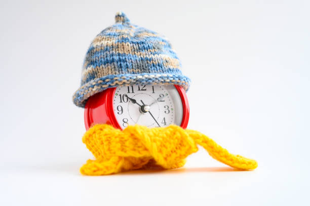 istock red round alarm clock in knitted wool blue hat and yellow scarf centered on a white background. winter time concept. winter season. cozy and warm. analog time 10:10 1187364149