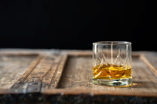Whisky glass with golden shimmering scotch on a brown used shabby barrel