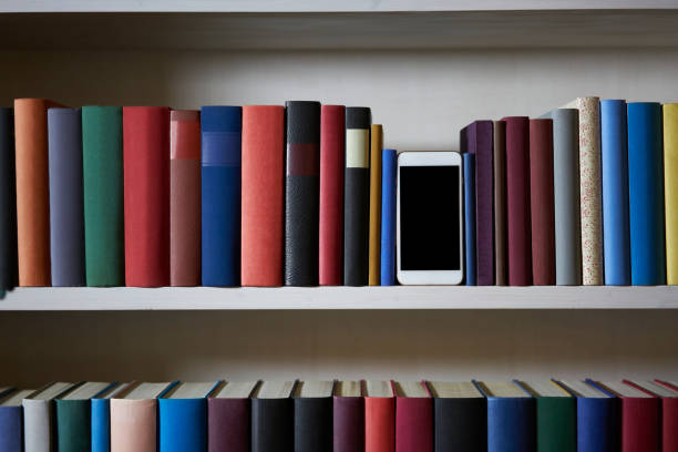 istock Mobile phone between books in a colorful bookshelf 1187371460