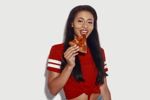 istock Attractive young woman eating pizza and looking at camera while standing against grey background 1187372914