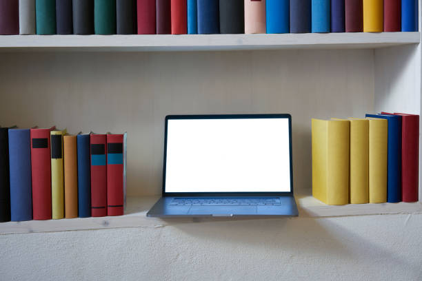 istock Open laptop with blank screen in a bookshelf with colorful books 1187373800