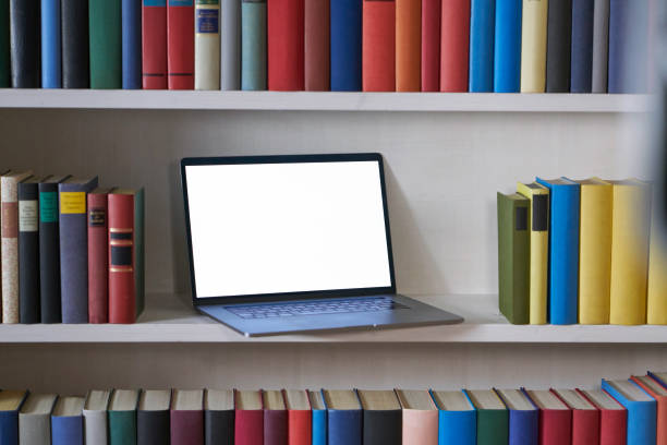 istock Open laptop with blank screen in a bookshelf with colorful books 1187373904