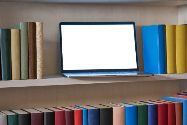 istock Open laptop with blank screen in a bookshelf with colorful books 1187374204