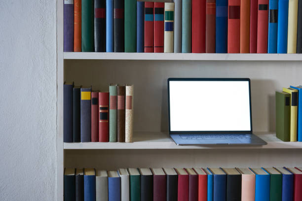 istock Open laptop with blank screen in a bookshelf with colorful books 1187374254
