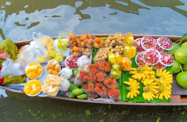 Photo of Local people sell fruits, food and souvenirs on boats at Damnoen Saduak Floating Market in Ratchaburi District, Thailand. Famous Asian tourist attraction.