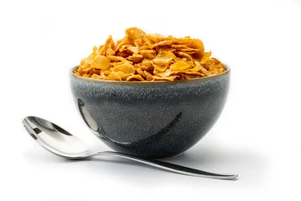 bowl filled with corned flakes and spoon, isolated on a white background